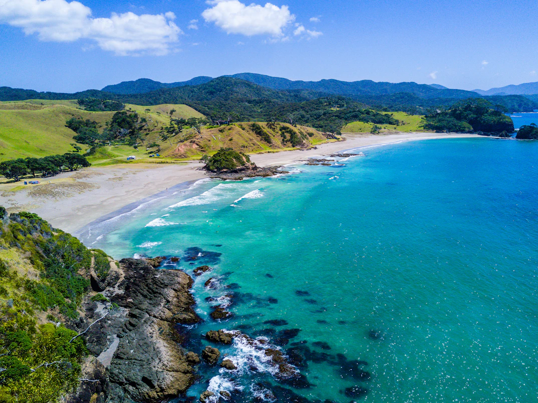 Baie de sable clair et mer turquoise au pied de collines vertes
